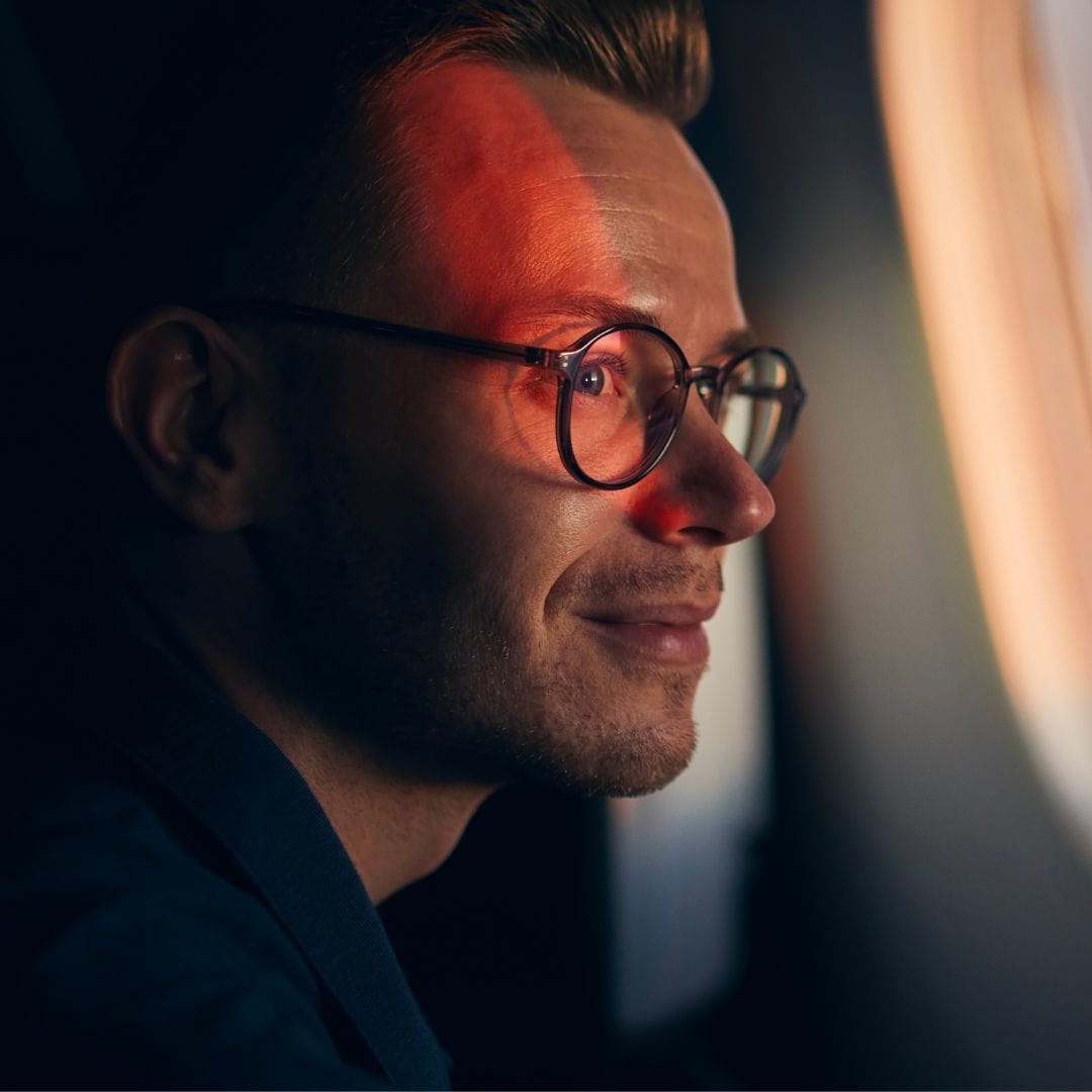 Serene passenger gazing through an aircraft porthole at a warm sunset reflected on his face.